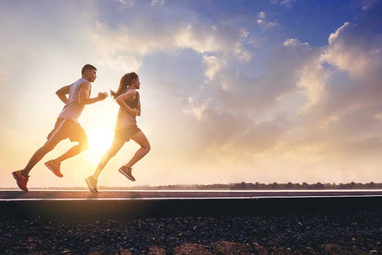 Young Asian couple in sports attire running together on an open road while the sun shines in the background