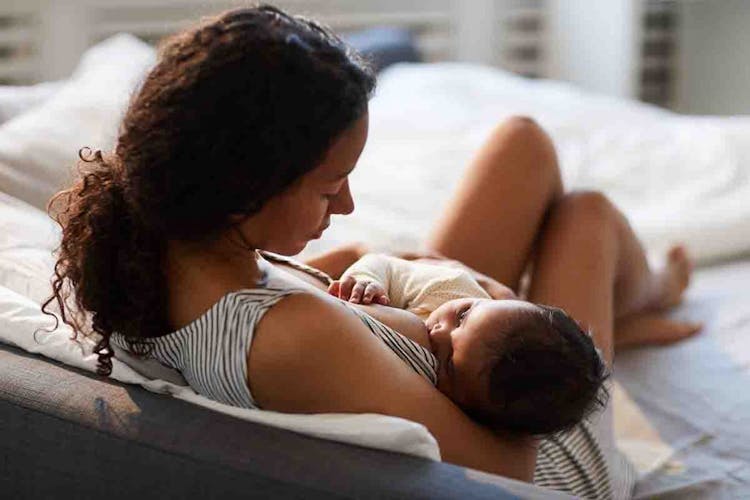 A mother breastfeeds her baby while sitting on her bed