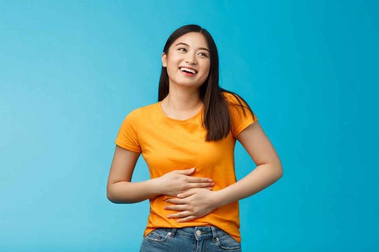 A happy woman in an orange t-shirt touching her stomach with her hands