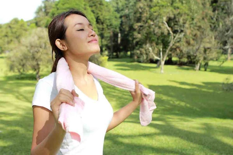  A fit woman holding a pink towel on her neck while jogging outside 