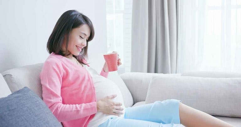 A happy pregnant woman drinking from a mug at home