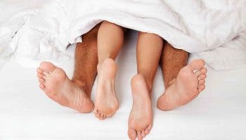 A man and woman sticking their legs from under the bedcover