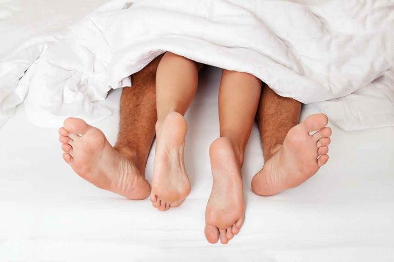 A man and woman sticking their legs from under the bedcover