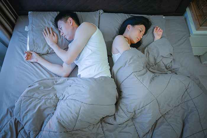 Asian couple looking sad and putting their back against each other in bed