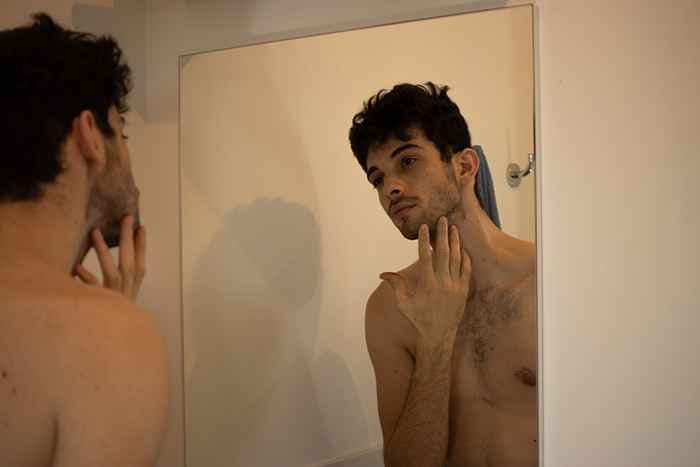 A man staring at his reflection in the mirror, checking his skin problems