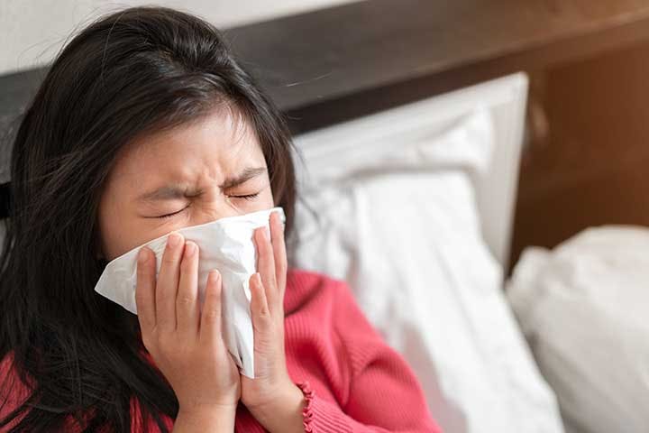 A girl sitting up in her bed as she sneezes into a handkerchief