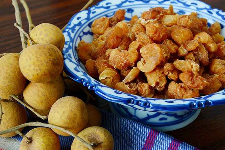 Fresh longan fruit next to a bowl of dried longan fruit