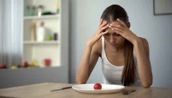 Thin woman in distress as she looks at a piece of fruit on a plate