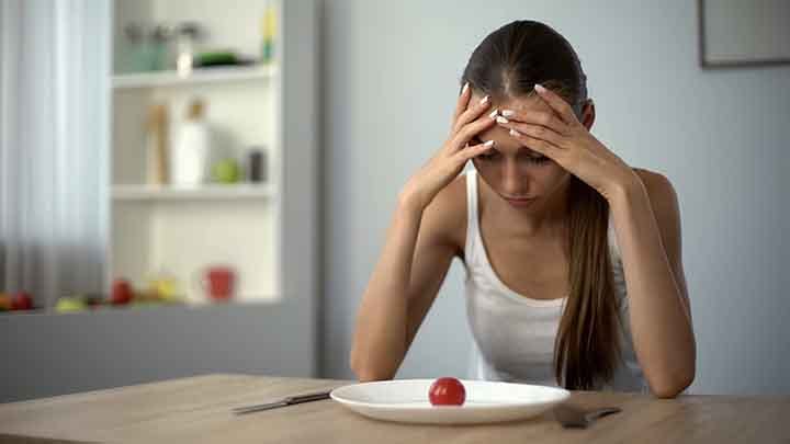 Thin woman in distress as she looks at a piece of fruit on a plate