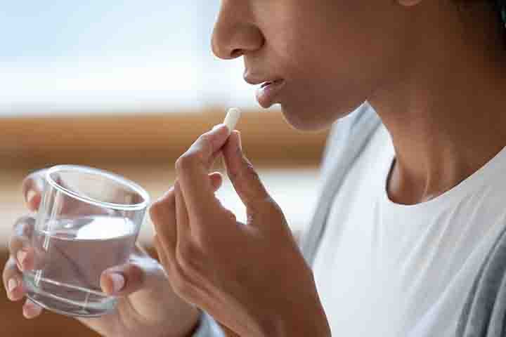 Woman about to take a pill while holding a glass of water in her hand