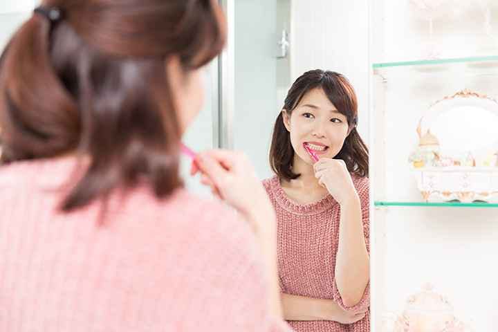 Woman smiling as she brushes her teeth while looking at her reflection in the mirror