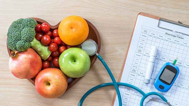 Plate of fruits and vegetables next to medical clipboard, blood glucose monitor, insulin pen, and stethoscope