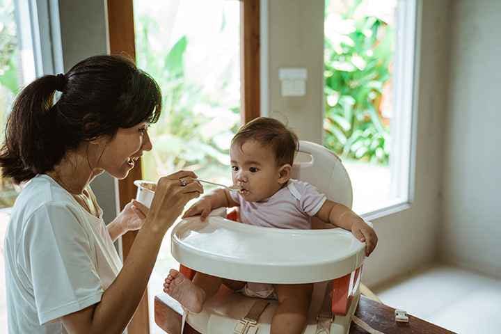 Woman feeding a baby that’s sitting on a high chair