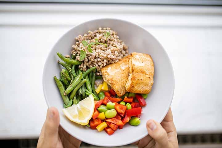 A plate of healthy food consisting of salmon, beans, vegetables and a slice of lemon 