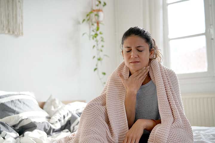 Woman with throat pain sitting up on the edge of the bed.
