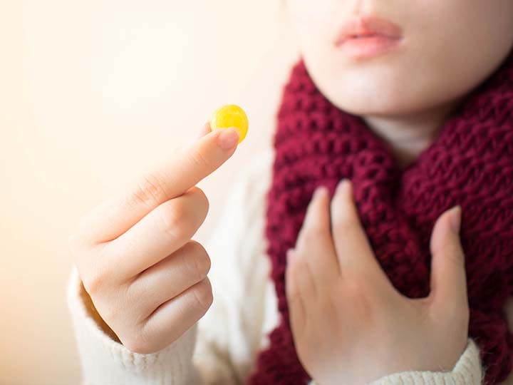 Woman taking yellow lozenges with her hands around her scarf.
