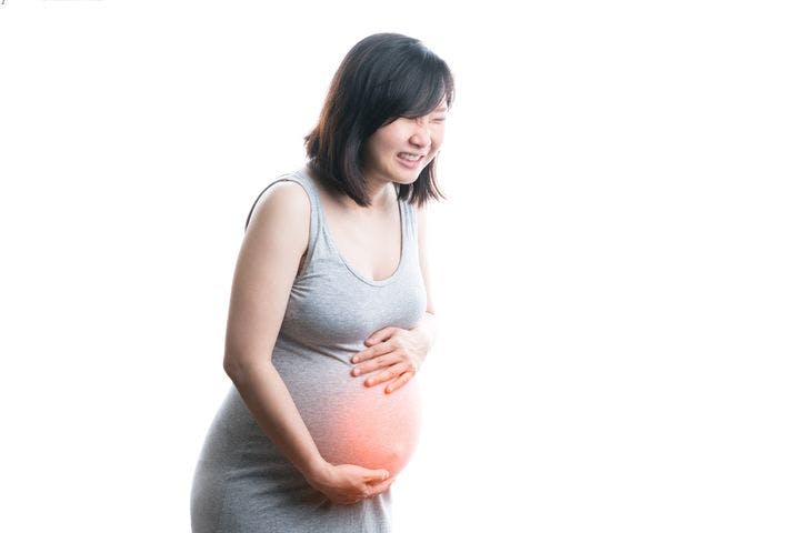 Asian pregnant woman holding her baby bump with pain and suffering expression on her face