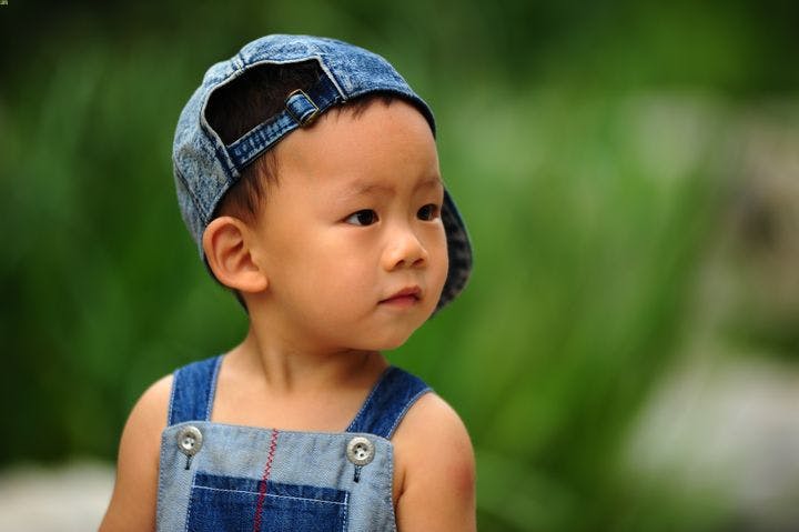 A boy wearing a denim cap and jumpsuit staring into the distance