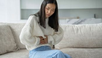 An Asian woman feeling abdominal pain while sitting on a sofa.
