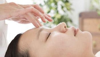 A close-up view of a woman’s face as she receives an acupressure massage between her eyebrows