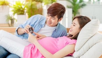 A young couple looking at an ultrasound photo while lounging on a couch
