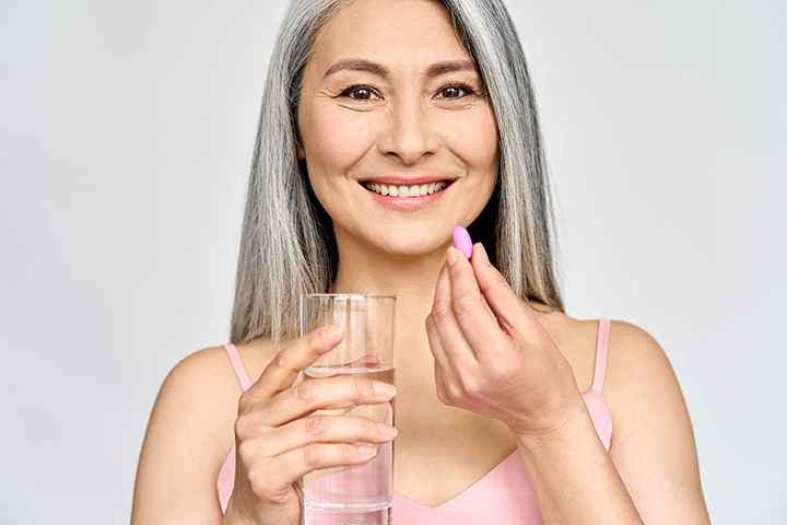 Asian older woman taking a medicine capsule with a glass of water in hand