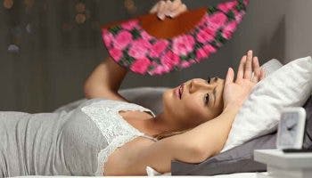 A woman fanning herself in bed due to excessive sweating