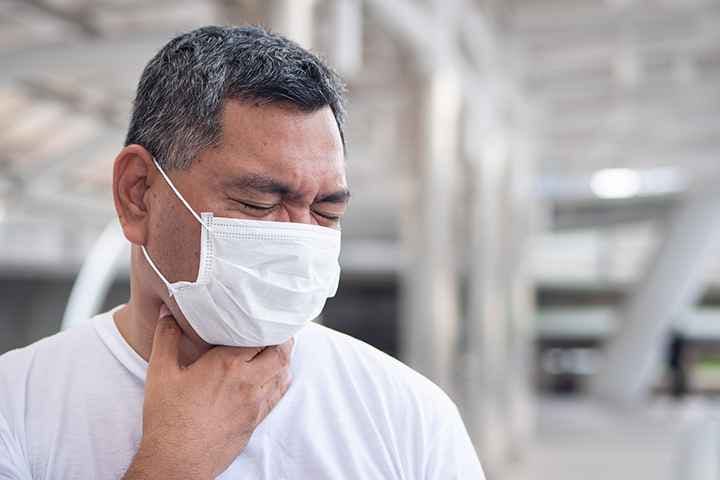 Asian man with mask coughing and having a sore throat