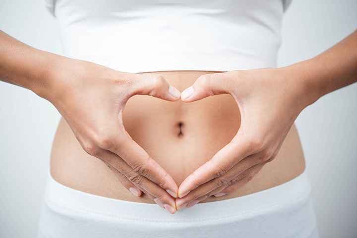 Woman holds hands in heart shape in front of her stomach