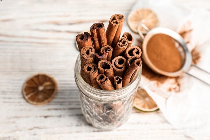 Cinnamon sticks in a small mason jar on a table next to a strainer filled with cinnamon powder