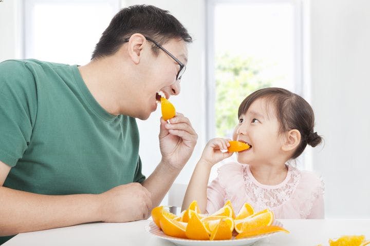 A young father is eating orange slices with his young daughter