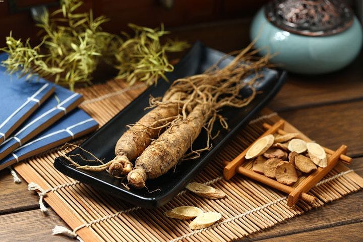 Two pieces of ginseng displayed on a black tray with ginseng slices on a bamboo mat