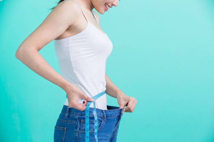 Woman using her right hand to hold a measuring tape around her waist and left hand to hold her jeans