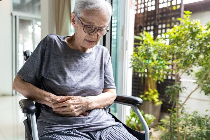 Elderly Asian woman in wheelchair with pain in her abdomen.