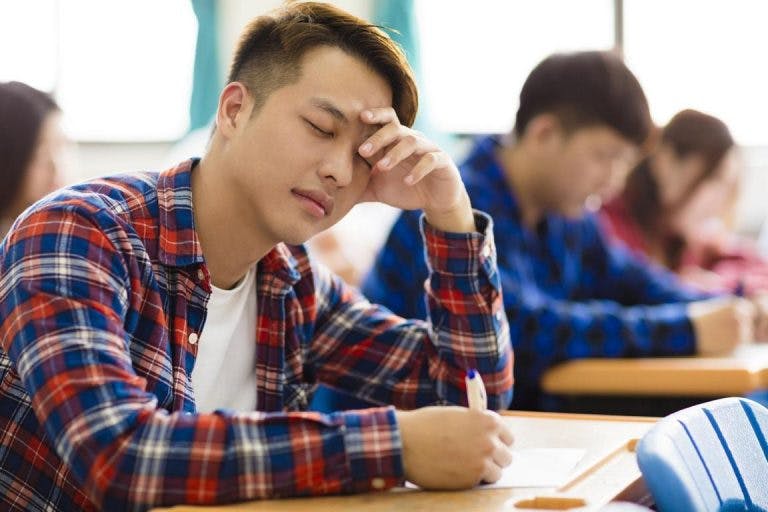 A male asian student feeling the low blood sugar symptoms in class