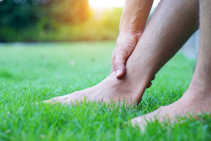 Man holding his right ankle while planting his feet on the grass