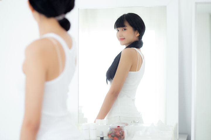 A young woman smiling while checking out her body shape in front of a mirror.