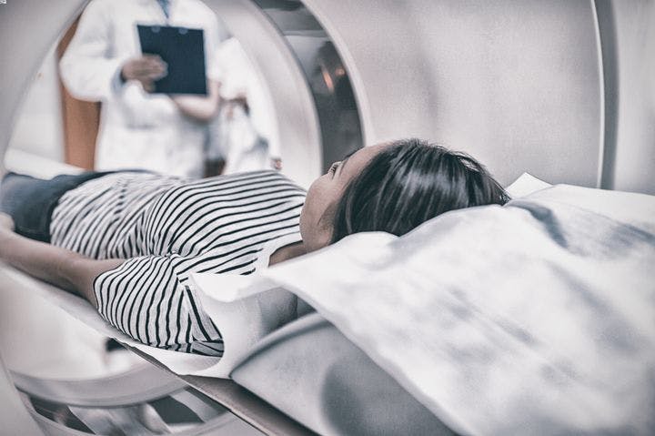 Woman lying supine as she enters a CT scan machine as a physician and nurse are seen in the background