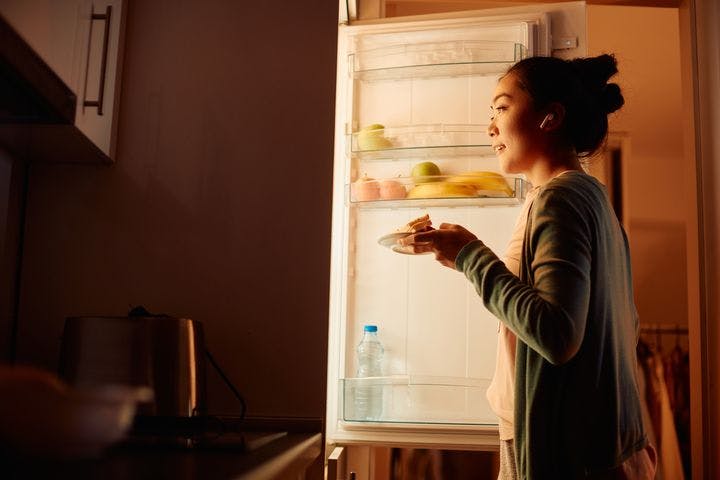 A woman standing in front of an opened refrigerator in a dark kitchen.