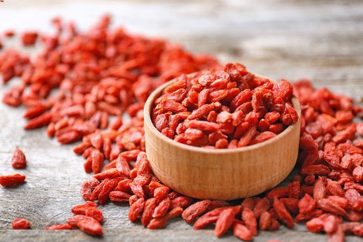 A small bowl of goji berries surrounded by pieces of scattered goji berries.