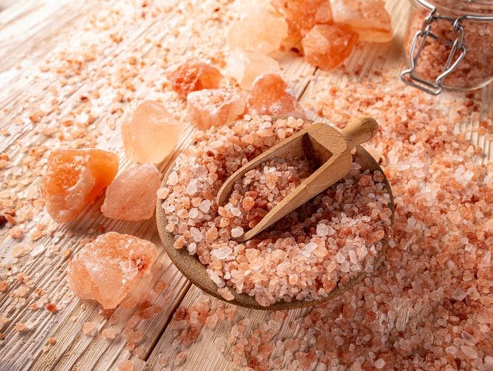 Himalayan salt in a bowl, big chunks of pink crystal on a wooden surface