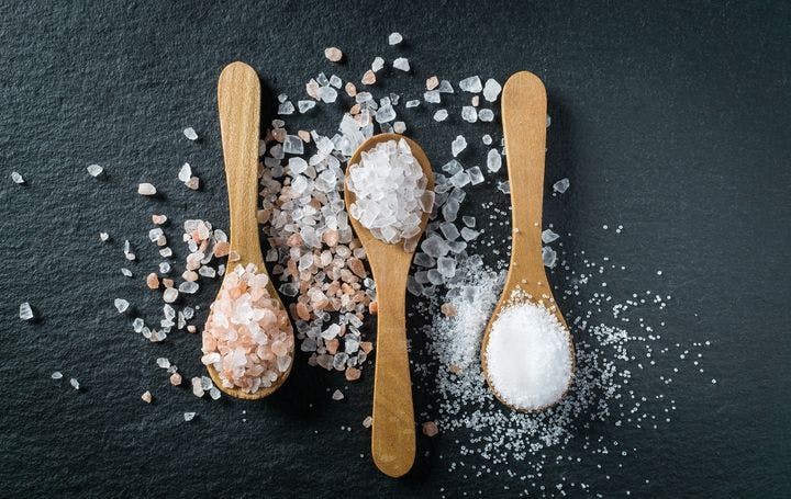 Different types of salt. Sea, Himalayan and kitchen salt on three wooden spoons against black background
