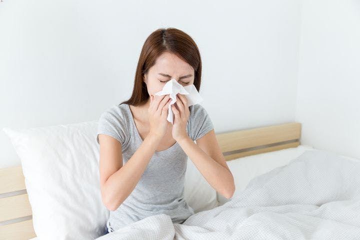 Woman feeling unwell and sneezing on bed