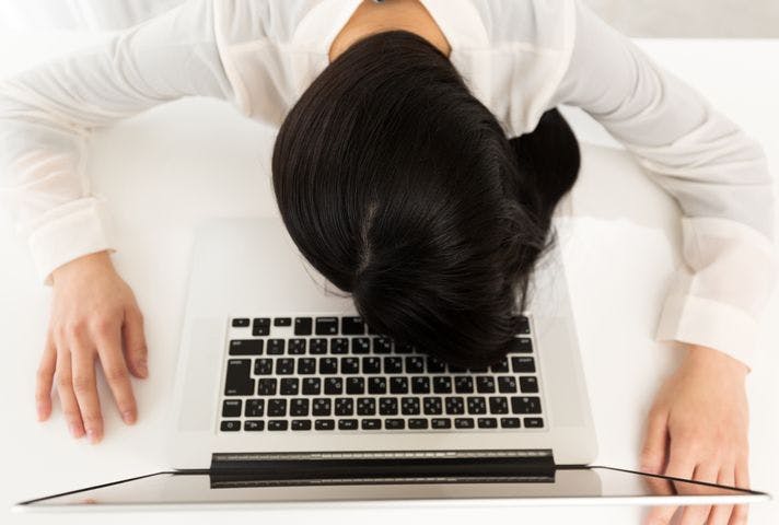An overhead view of a female employee with her face down on her desk on top of her laptop.