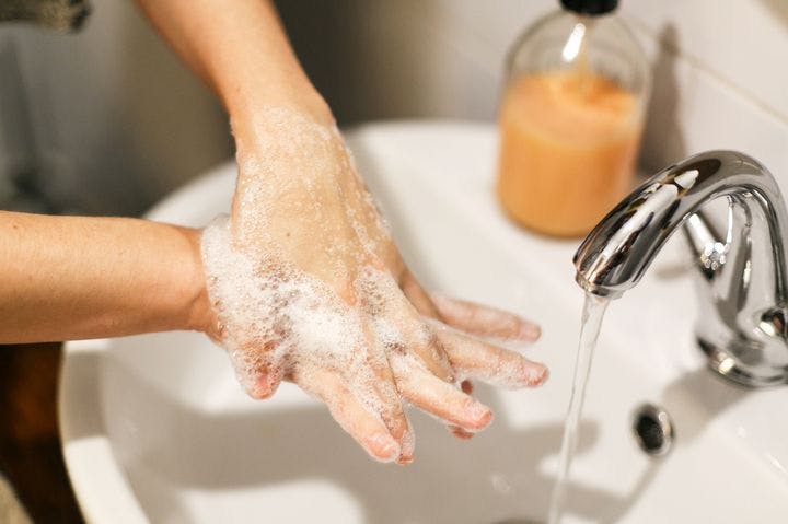 A partial view of a pair of hands in the midst of being washed with soap and water running from a faucet