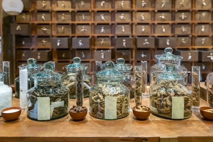 Glass jars and plastic bowls containing herbal ingredients displayed on a wooden table 