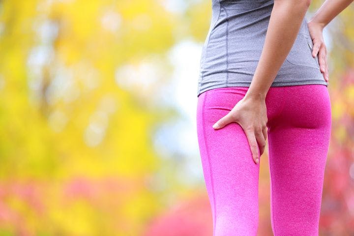 Woman using her left hand to hold her left hamstring while standing