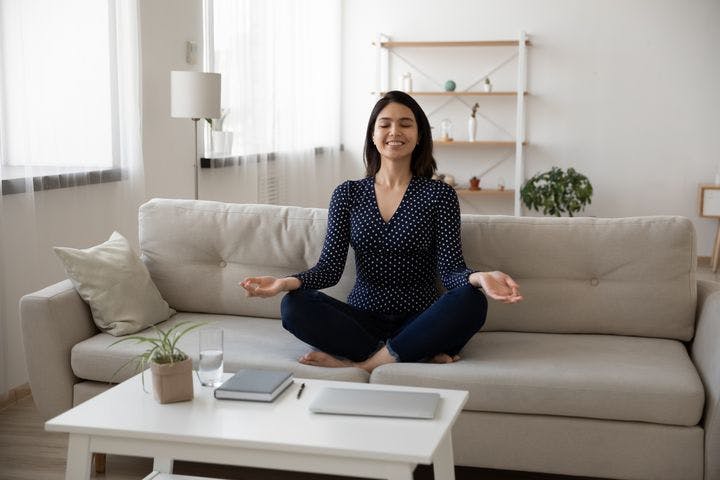Woman sitting on a sofa smilingly with folded legs and her wrists on her knees