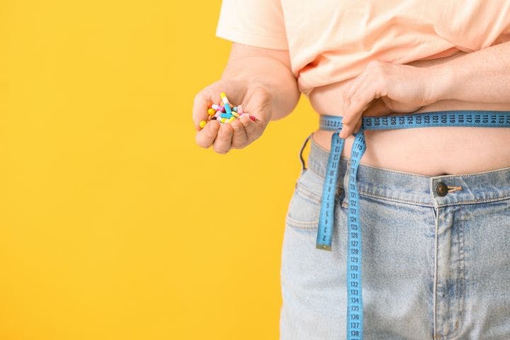 Woman holding weight loss pills and measuring tape