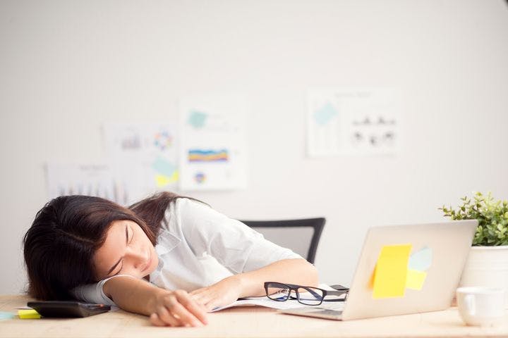 A female employee sleeping on her desk, surrounded by her laptop and other items.
